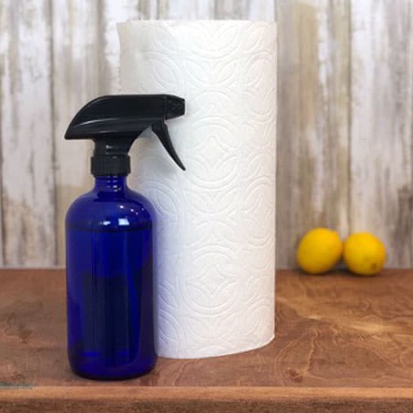 blue spray bottle and paper towels with lemons in background