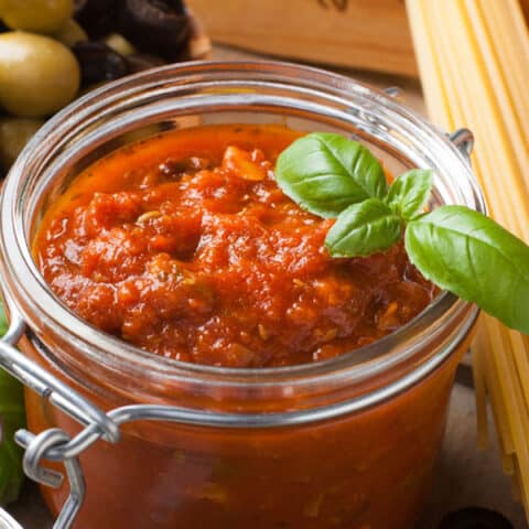 glass jar full of chunky spaghetti sauce garnished with basil leaves