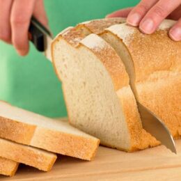 person slicing loaf of white sandwich bread