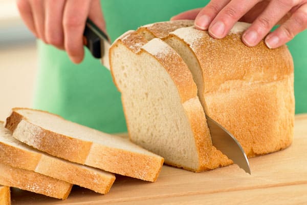 person slicing loaf of white sandwich bread