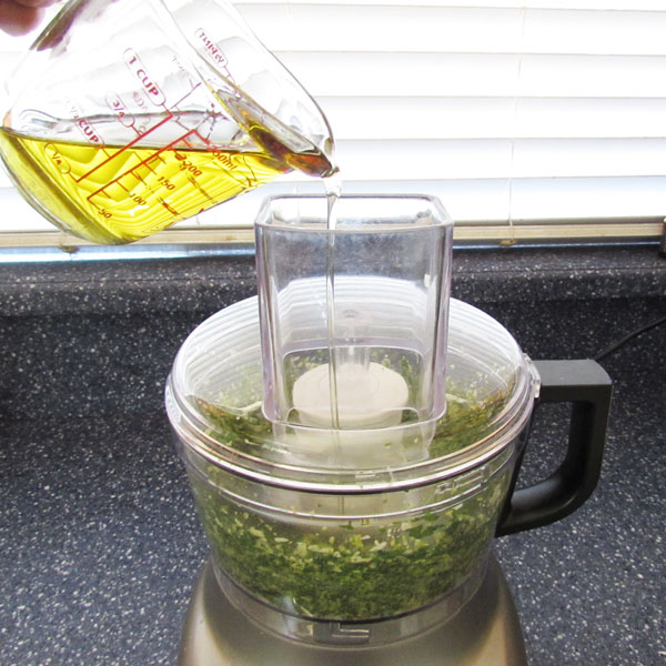 adding olive oil to pesto in food processor