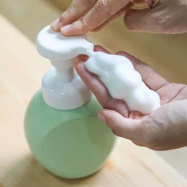 closeup of woman dispensing foaming hand soap from green ceramic container