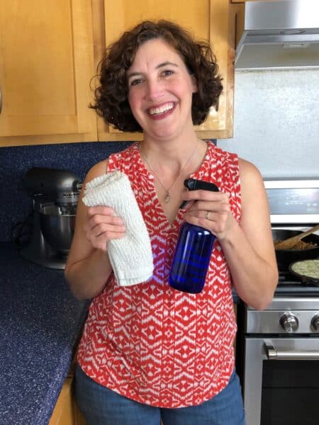 woman smiling in kitchen holding cloth and spray bottle