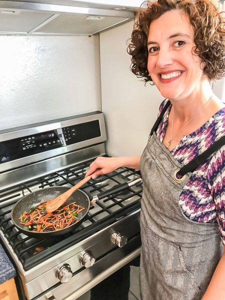 woman smiling and cooking stir fry vegetables at stove