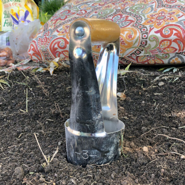 bulb planting tool in soil with colorful pillow in background
