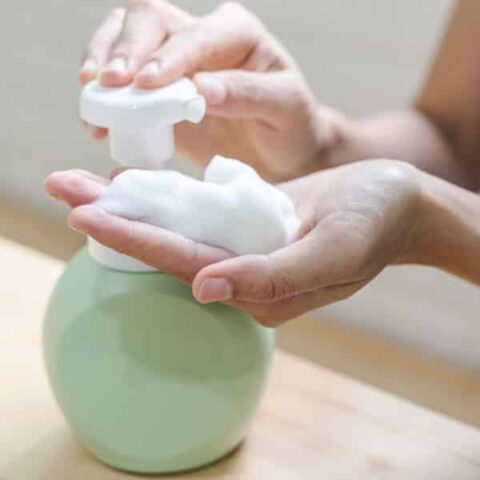 woman dispensing foaming hand soap from green ceramic container
