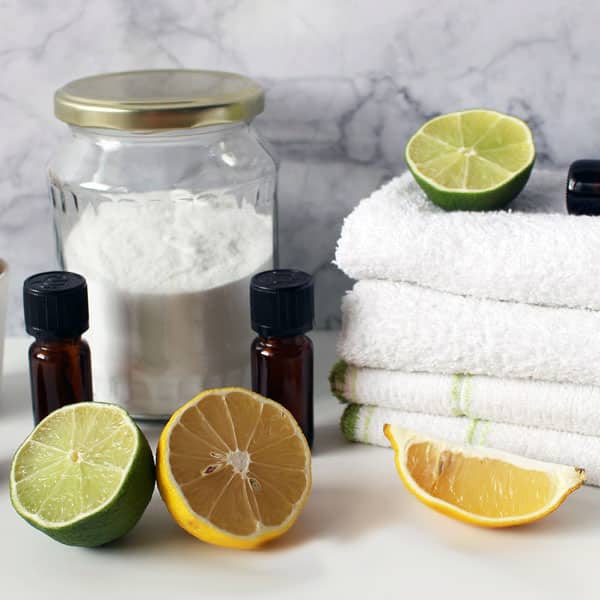 essential oils, lemon, lime, baking soda, cloths on white table