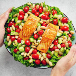 hands holding platter of salmon and tomato salad