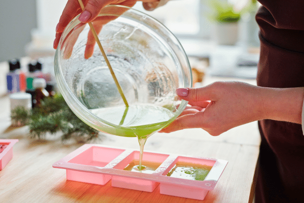 green soap being poured into pink silicone soap mold