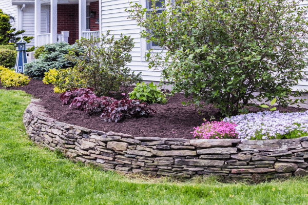 flowers and herbs in raised garden bed with rock wall