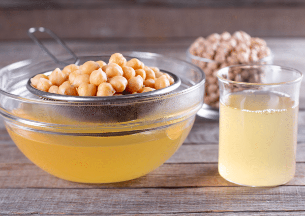 chickpeas in a strainer over a bowl of aquafaba (chickpea canning liquid)